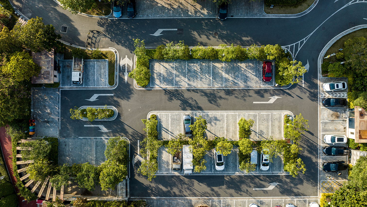 Aerial view of a parking lot with parked cars and trees between the rows.